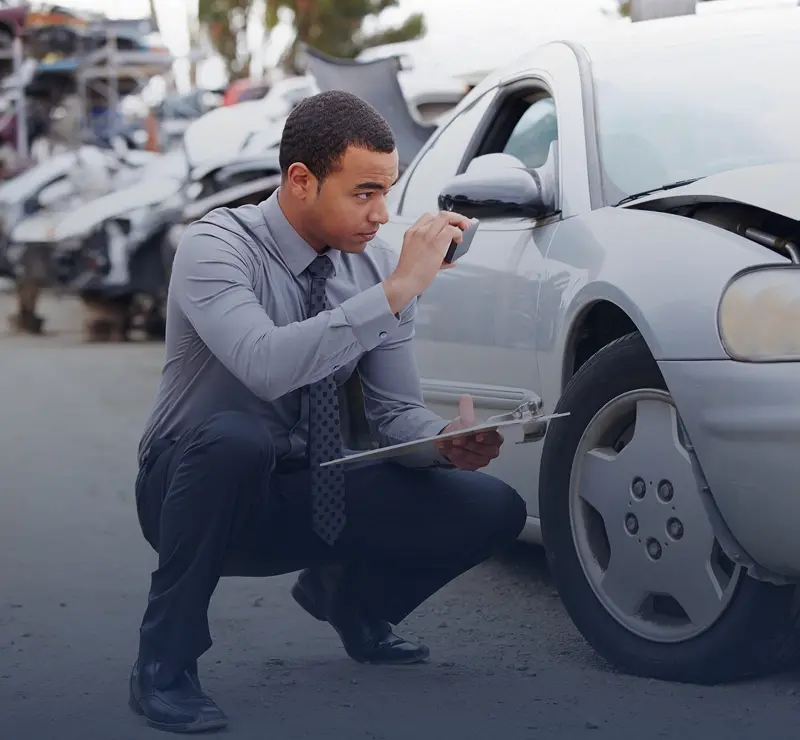 Man inspecting damaged car with clipboard.